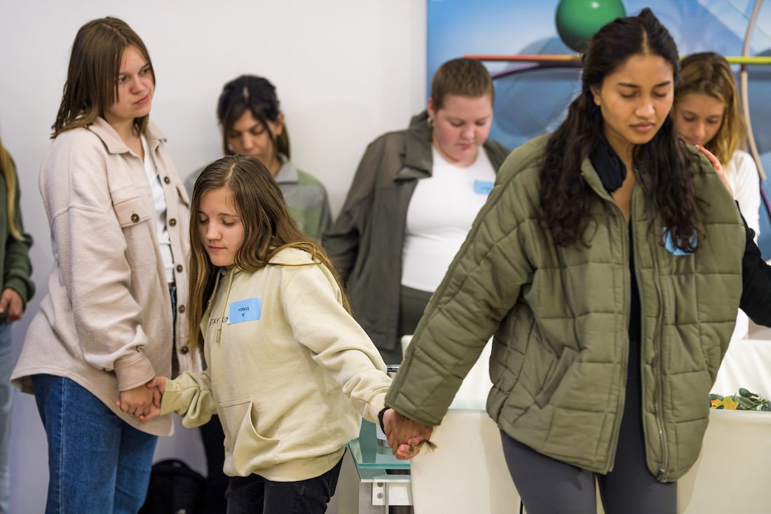 Ellice and other young women hold hands to pray before sitting down for dinner at the retreat.