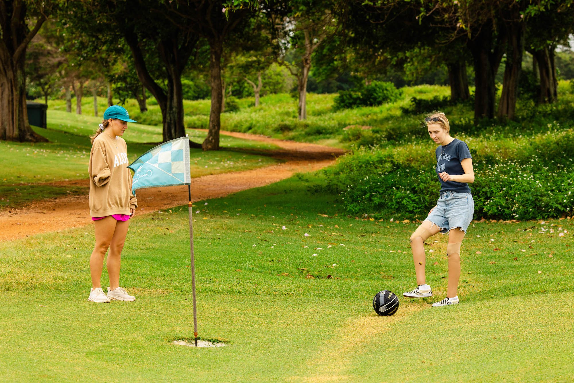 Double leg amputee kicking a soccer ball into the footgolf course hole