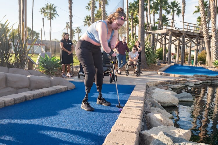 Quad amputee Evelyn gets ready to adaptively swing her golf club during an afternoon of mini golf.