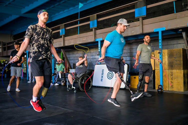 Three Forge retreat attendees and leg amputees jump rope in a CrossFit gym using RX Smart Gear's adaptive ropes.