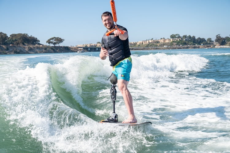 Forge attendee and leg amputee Josh smiles and gives a shaka standing up for the first time wakesurfing.