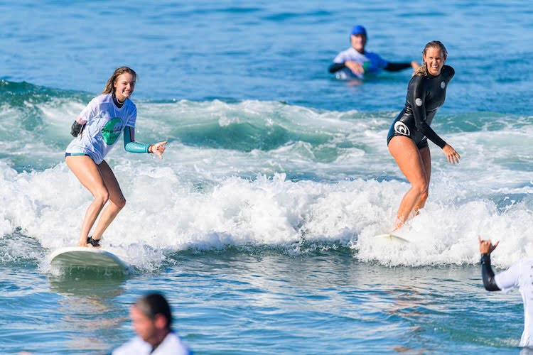 Beautifully Flawed attendee Devyn catches a wave alongside Bethany Hamilton and the two ride their surfboards together to shore.