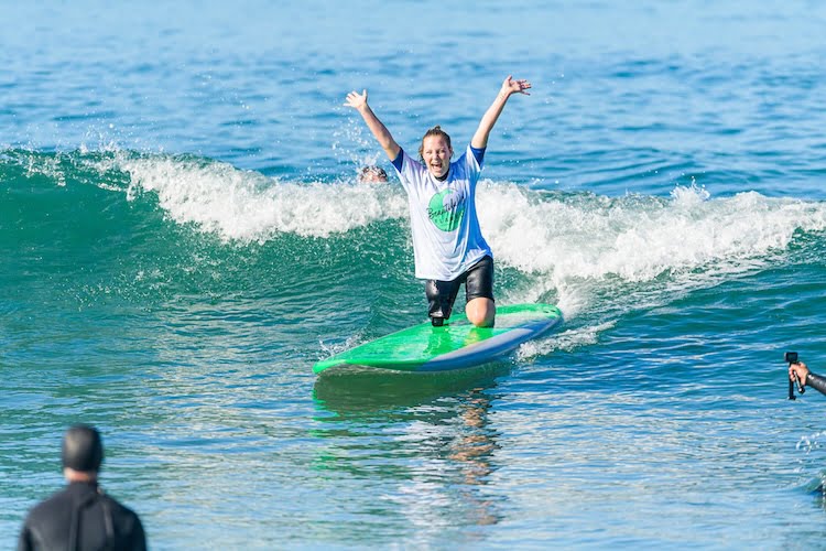 Attendee Emma June ecstatically throws her arms in the air when she catches a wave and surfs to shore.