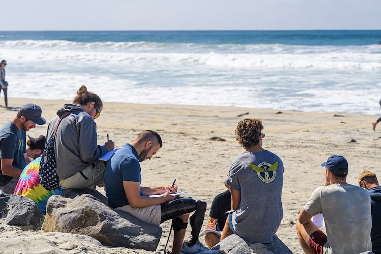 The Forge men sit on the beach for their group session while working on their workbooks after a discussion.