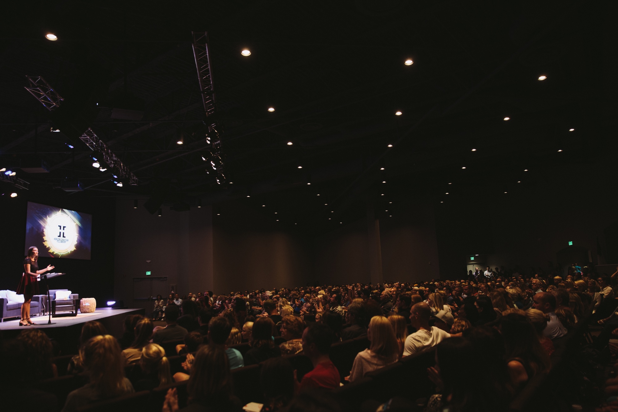 A woman speaks on stage to a packed audience at a Beautifully Flawed Foundation event.