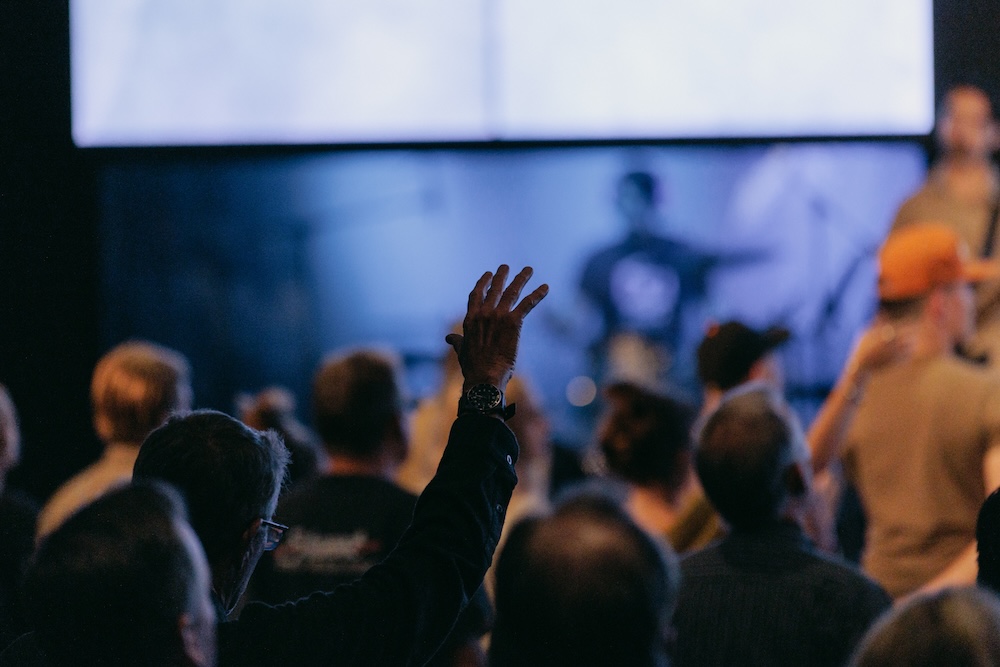 A person raises their hand in worship or response during a Shine Forth worship session.