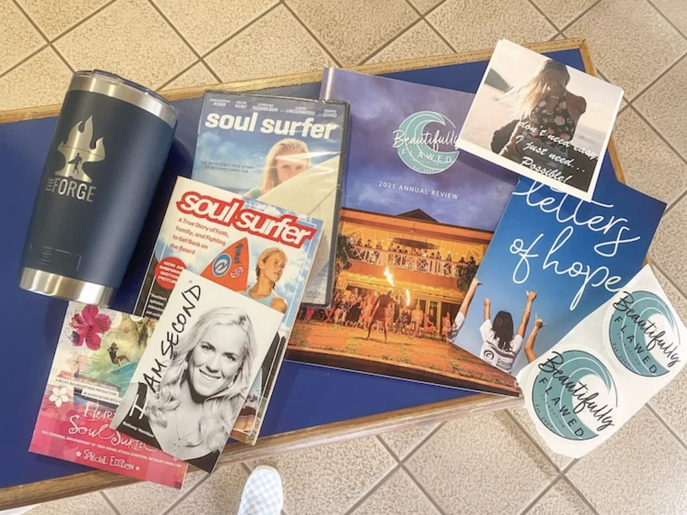 A collection of Beautifully Flawed Foundation resources and merchandise, including Soul Surfer books, stickers, a tumbler