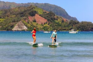 Two surfers ride small waves side by side during an adaptive surfing lesson in tropical waters.