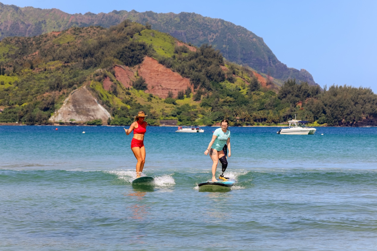 Two surfers ride small waves side by side during an adaptive surfing lesson in tropical waters.